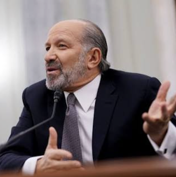 A bearded man in a dark suit and patterned tie gestures with both hands while speaking into a microphone, appearing to testify or speak at a formal hearing.

The image likely relates to the post by depicting Howard Lutnick, the US Commerce Secretary mentioned in the article, during one of his public appearances or testimonies.