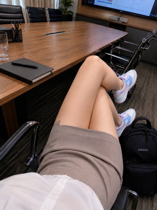 A pair of long legs crossed at the knee resting under a conference table, paired with a black Samsung backpack and a notebook with a pen, fitting the caption's playful boast about having "long legs" and earning an extra $200 plus one content piece for NBL.