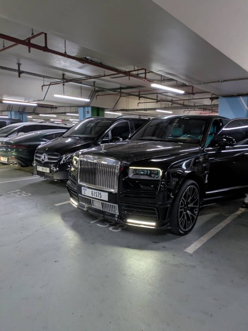 A black Rolls-Royce Cullinan with license plate 61575 parked in an indoor garage next to a Mercedes-Benz.