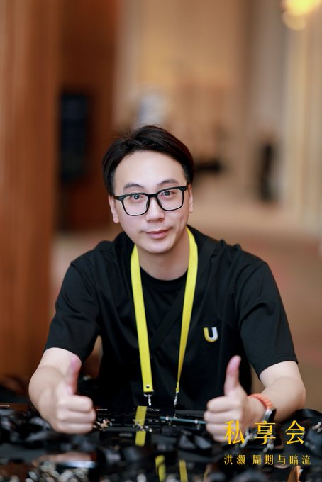 A man wearing glasses and a black shirt with a "U" logo gives two thumbs up while seated behind what appears to be a mechanical keyboard setup, with text "私享会" (Private Gathering) and Chinese subtitle visible. The image corresponds to the Binance VIP Private Gathering post, suggesting he attended this exclusive event as a special guest.