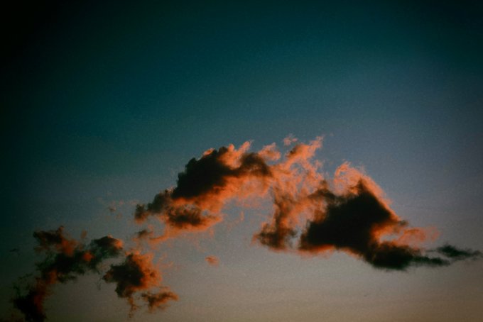 Dark clouds with pinkish-orange highlights are silhouetted against a gradient teal and peach sky at dusk or dawn.