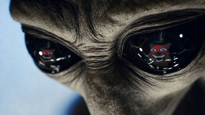 A close-up of a grey alien's face, featuring large black eyes that reflect two small cartoonish red creatures with wide, toothy grins.