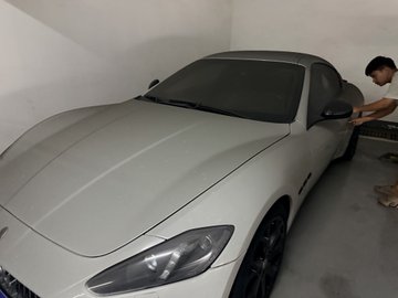 A light green luxury sports car (appears to be a Maserati) parked in a garage with a person standing beside it.