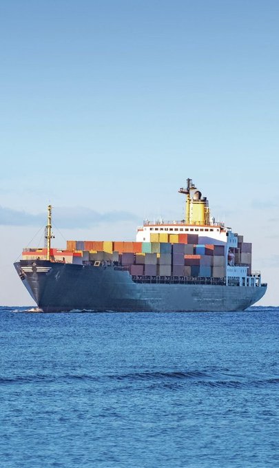 A large container ship loaded with colorful shipping containers sails on a calm blue ocean.