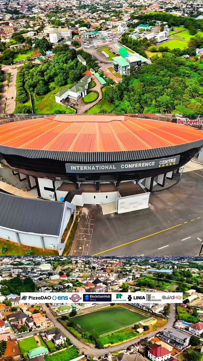 The image shows an aerial view of a large stadium with a red roof, surrounded by green trees. The stadium appears to be hosting an event or conference, as indicated by the text "International Conference" written on its roof. The image also includes a photo of a small town in Enugu, Nigeria, which is part of the same country where the stadium is located. This suggests that the event might have been held in Enugu during the year 2006.