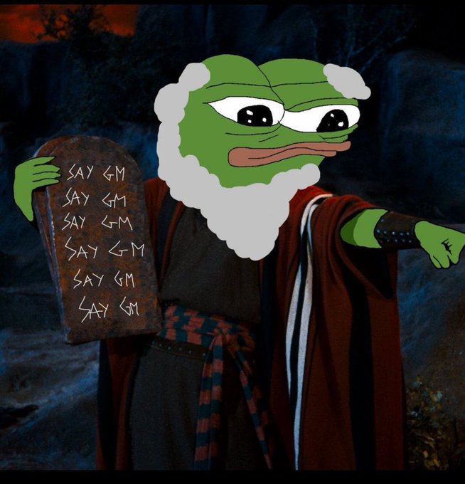 A meme featuring a Pepe the Frog face edited onto a Moses-like figure holding stone tablets inscribed with 'SAY GM' repeatedly, set against a dramatic rocky background.
