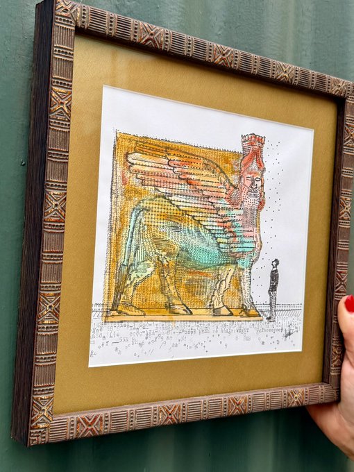 A framed artwork depicting a colorful winged bull-like mythical creature with a human face, held up against a green wall.