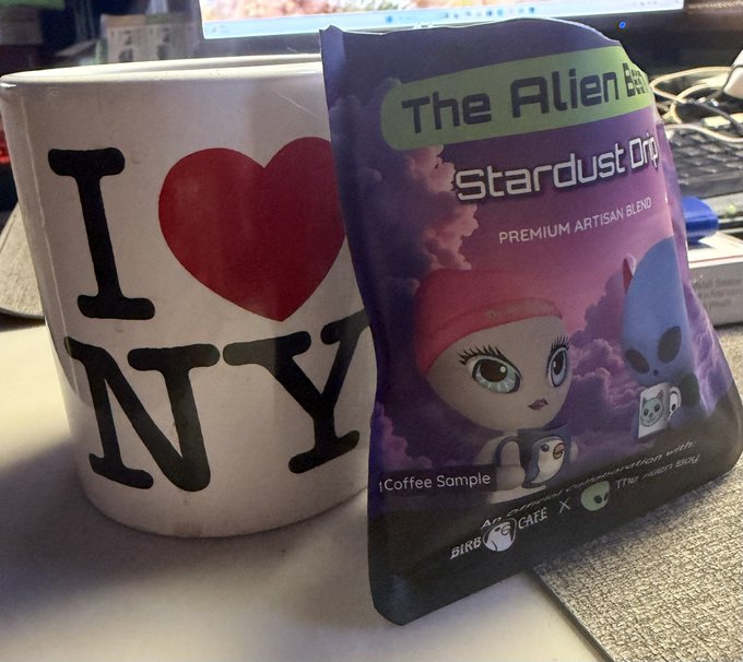 An 'I ❤️ NY' white mug sitting next to a purple coffee bag labeled 'The Alien Blues - Stardust Drip - PREMIUM ARTISAN BLEND' with cartoon characters, marked '1 Coffee Sample' and 'An EPIC Collaboration with BIRD x CAFE x The First Brew'.