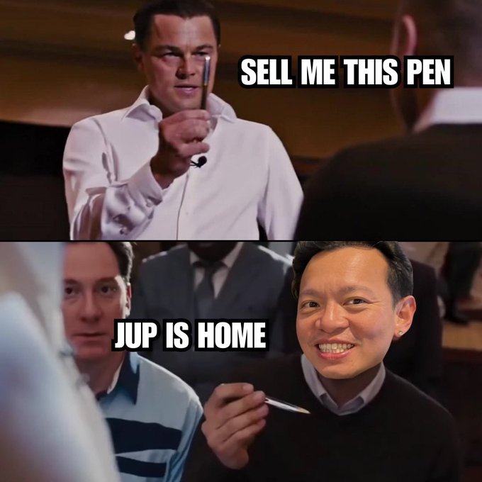 A two-panel meme from *The Wolf of Wall Street* showing Leonardo DiCaprio holding a pen with text "SELL ME THIS PEN," while the bottom panel shows a smiling man holding a pen with text "JUP IS HOME," humorously reframing the pen as a JUP token being unshakeable and refusing to be sold, matching the post's "I'M NOT LEAVING" sentiment.