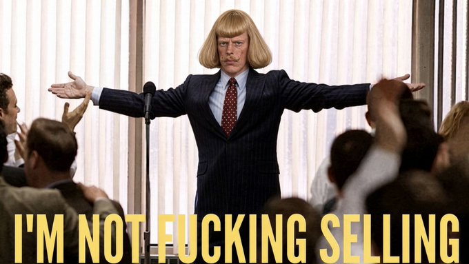 A movie still shows a man with a blonde bob haircut in a red tie standing with arms outstretched, with the text "I'M NOT FUCKING SELLING" overlaid in large yellow letters.