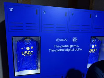 A blue locker display at Circle's pop-up house features USDC-branded jerseys in numbered lockers (8, 9, and 10), promoting "The global game. The global digital dollar." alongside the USDC and Circle logos. The image captures the branded merchandise and promotional messaging from Circle's activation at Token2049 in Singapore, highlighting their stablecoin initiative ahead of upcoming Arc events in Lisbon.