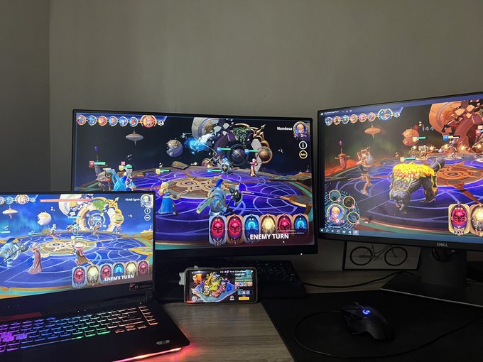 A multi-screen gaming setup showing a fantasy game being played simultaneously on a laptop, a smartphone, and two external monitors, with 'ENEMY TURN' visible on the displays.