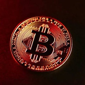 A close-up image of a physical Bitcoin coin illuminated with a reddish glow.