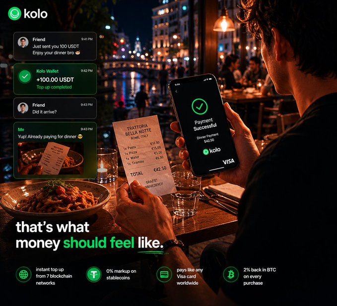 The image shows a person sitting at a table in a restaurant holding up their phone displaying a payment app that says "KOLO". The person appears to be using the app to send money or make a purchase, possibly for dinner with friends. The scene takes place in a restaurant setting where there are other people present but not visible in the image.