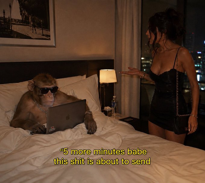 A surreal AI-generated meme showing a monkey wearing sunglasses and a chain, using a MacBook on a hotel bed, with caption text '5 more minutes babe this shit is about to send'.