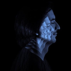 A dramatic side-profile portrait of a man with long dark hair illuminated by blue light against a black background, featuring a surreal geometric texture on his face.