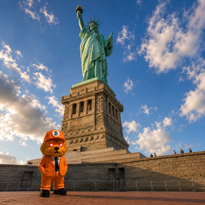 An artistic composite image showing a dog mascot wearing an orange Bitcoin cap and suit standing in front of the Statue of Liberty.