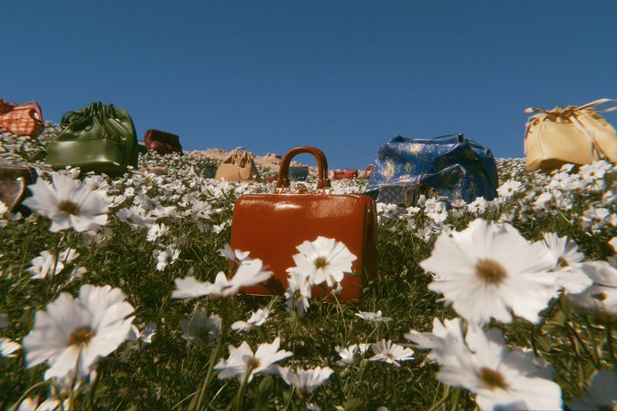 Artistic photograph showing various vintage handbags placed in a field of white daisies under a clear blue sky.
