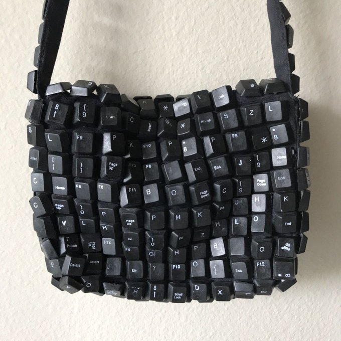 A black handbag constructed entirely from various computer keyboard keys is displayed against a white wall.