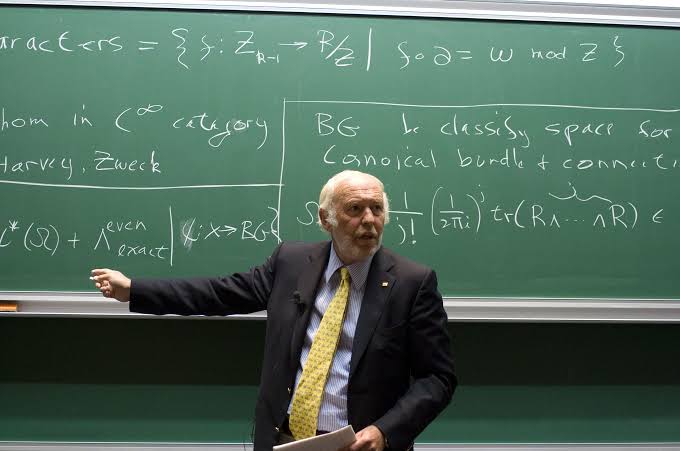 The image is completely unrelated to the post about Renaissance Technologies and Bitcoin. It shows an older man in a dark suit and yellow tie lecturing in front of a green chalkboard filled with advanced mathematics notation, including references to "Harvey, Zweck," "BG," and a formula involving "tr(R₁...R₁)."

The juxtaposition is clearly a meme designed to mock the post—using a distinguished mathematics professor to sarcastically suggest that the math behind Renaissance Technologies' $222 million $MSTR investment is extraordinarily complex and impressive.