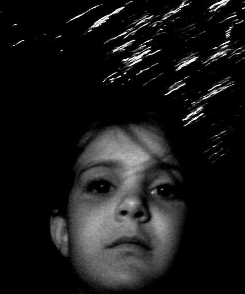 A grainy black-and-white close-up of a young child's face illuminated against a dark background, with abstract streaks of light above their head. The image, posted by bitfossil.org, appears to serve as a creative, atmospheric visual rather than a literal Bitcoin-related graphic.