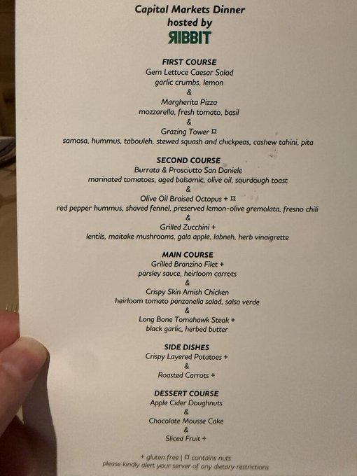 A menu from a "Capital Markets Dinner" hosted by Ribbit Capital, featuring a multi-course meal with dishes like Gem Lettuce Caesar Salad, Burrata & Prosciutto, Grilled Bronzino Fillet, and Apple Cider Doughnuts. The menu reflects the elegant dinner setting mentioned in the post, where Ribbit Capital gathered capital markets leaders to discuss their recent AI power bottleneck letter.