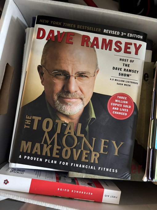 A paperback copy of "The Total Money Makeover" by Dave Ramsey, 3rd Revised Edition, sits in a bin, noting it's a New York Times Bestseller with over three million copies sold.