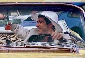 A scene from a movie or TV show featuring a man in a white cowboy hat smiling from the driver's seat of a convertible car.