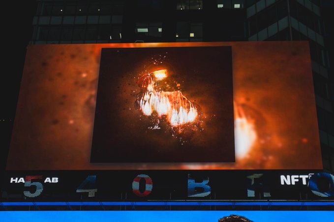 A large illuminated billboard displays a fiery, abstract digital artwork, with a digital ticker below showing text including '5', '4', '0', 'b', and 'NFT'.