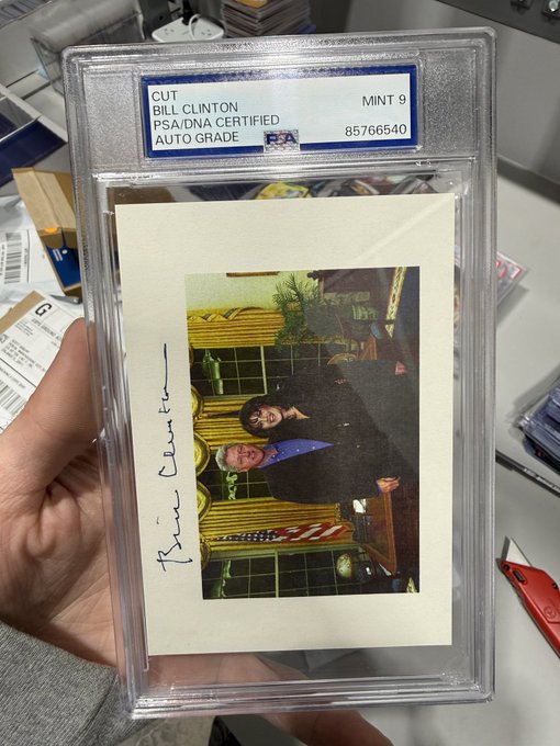 A PSA/DNA certified and auto-graded "MINT 9" Bill Clinton cut autograph (#85766540) displayed in a protective plastic case held by a hand.