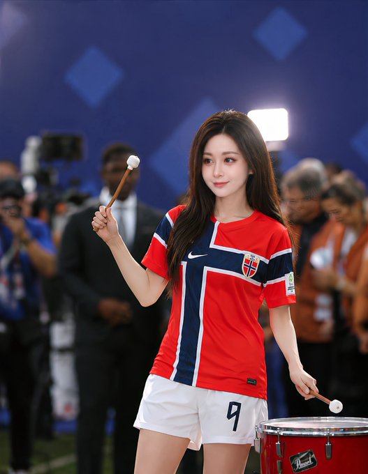 A young woman wearing a red and navy Norway football jersey with the number "9" on her white shorts holds drumsticks and stands beside a Pearl drum, with the post expressing conflicted support for England over Norway in a match while betting through OKX.