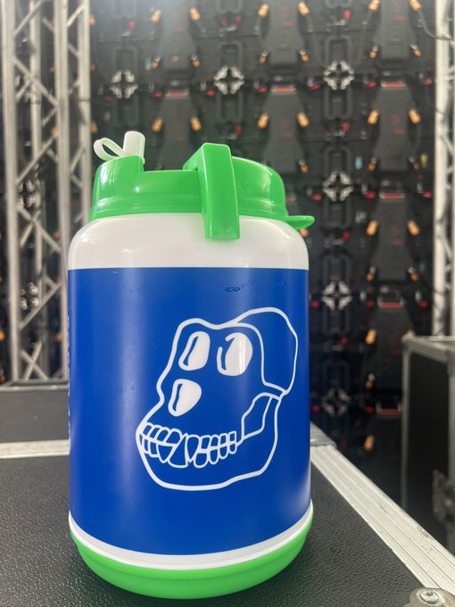 A blue and white insulated jug with a green lid featuring a cartoon skull design, sitting in front of LED video wall panels at what appears to be an event venue.