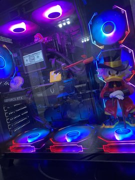 A photograph of the interior of a custom-built gaming PC case featuring illuminated RGB fans and a top hat-wearing anime figurine inside.