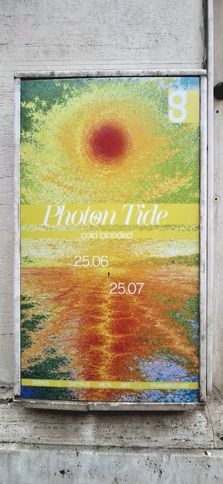 A framed street poster on a concrete wall titled 'Photon Tide - cold blooded' with dates 25.06 and 25.07, featuring a psychedelic sun-like graphic over a landscape.