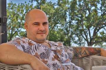 A bald man in a tropical shirt relaxes outdoors, fitting the relaxed "Solana Summer" vibe with sunshine and greenery in the background.