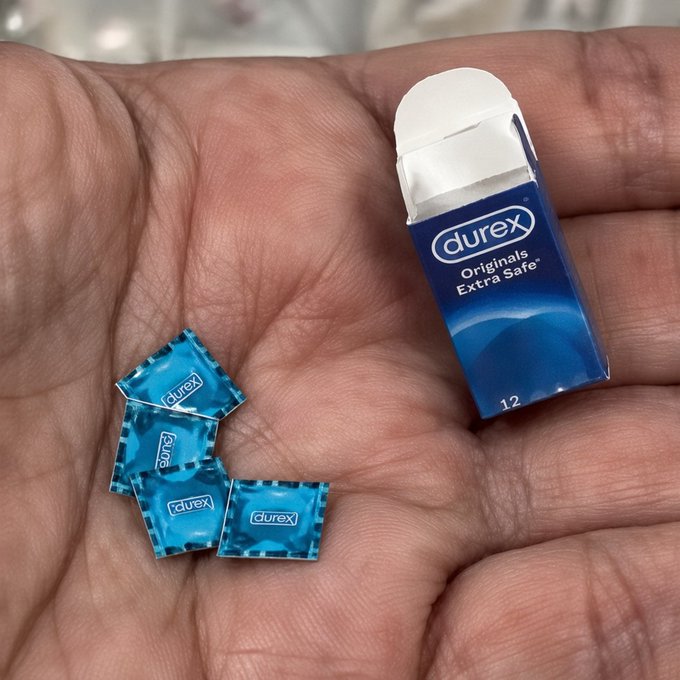A hand holds a miniature replica of a Durex Originals Extra Safe box (marked "12") alongside tiny blue condom wrappers, the tiny scale humorously reinforcing the post's caption "Vale is very good… bitcoin:native," where "Vale" (Spanish for "it's worth it") plays on "value," symbolizing that Bitcoin is worth investing in despite its small beginnings.