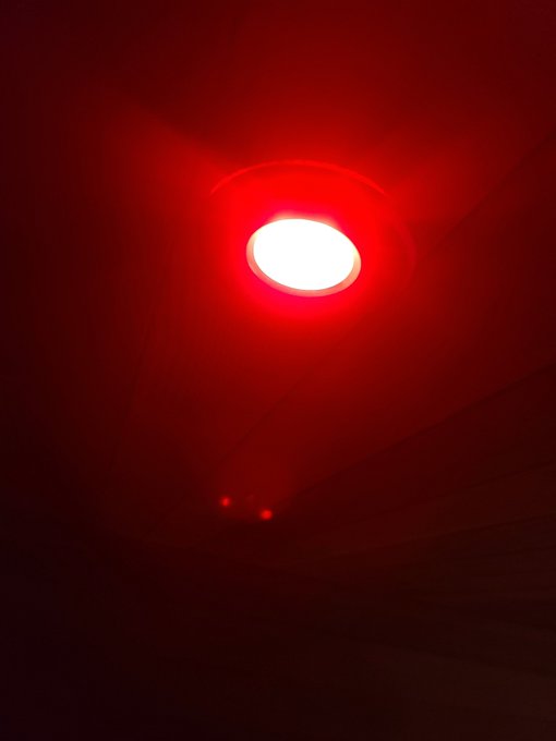 A ceiling-mounted light fixture glowing bright red in a dark room, with smaller red indicator lights visible below.