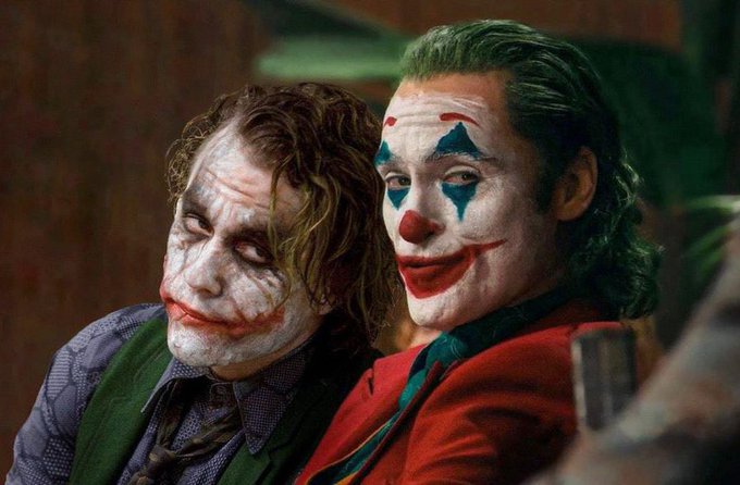 The image features two actors, one wearing a purple suit with a green tie and the other dressed in a red suit with a clown nose makeup style. They are sitting next to each other, both smiling at the camera. The caption below the image reads "how my btc and eth positions look at me when I check my portfolio".