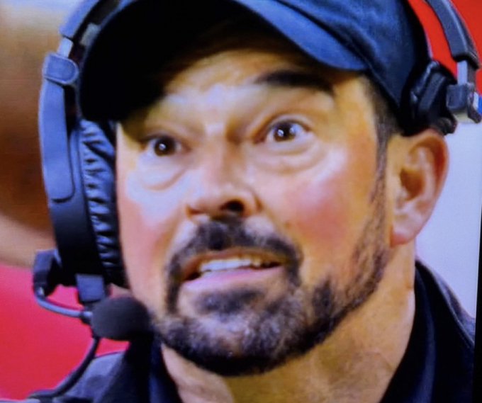 A close-up shot of a man wearing a dark cap and a headset microphone, looking intensely off-camera.