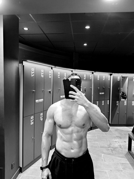 A shirtless man takes a mirror selfie with his phone in a locker room lined with numbered lockers (including 030, 031, 032, 033, 034, and others), seemingly documenting his post-workout physique before signing off for the night. The image's gym setting and "Good night CT" caption suggest he's wrapping up a late-night Connecticut workout session.