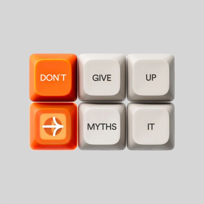Six computer keyboard keys arranged in a 2x3 grid spell out "DON'T GIVE UP" on the top row and an airplane icon, "MYTHS," and "IT" on the bottom row, with two orange keys contrasting against four white keys.