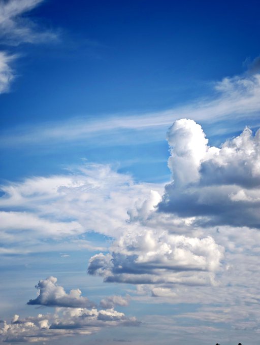 A photograph of a bright blue sky with scattered, fluffy white cumulus clouds.