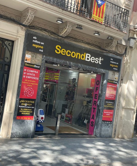The image shows the storefront of "SecondBest," a second-hand shop in Catalonia (indicated by the Catalan independence flag) advertising "les millors en segona mà" (the best in second-hand), with signs reading "COMPRA & VENTA & EMPEÑOS" (buy, sell, pawn) and "OFERTAS." The connection to the post appears to be a metaphor: just as this store specializes in second-best second-hand goods rather than top-tier items, the post suggests "Saylor lied to us!" — implying Saylor's promises were second-rate, secondhand, or not the genuine article.