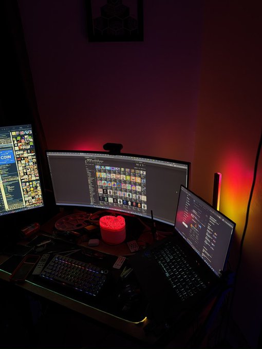 A trading desk setup with multiple monitors displaying financial charts and a Coinbase interface showing "COIN," alongside two keyboards and a glowing red lamp, reflects an active trading session with a positive outcome.