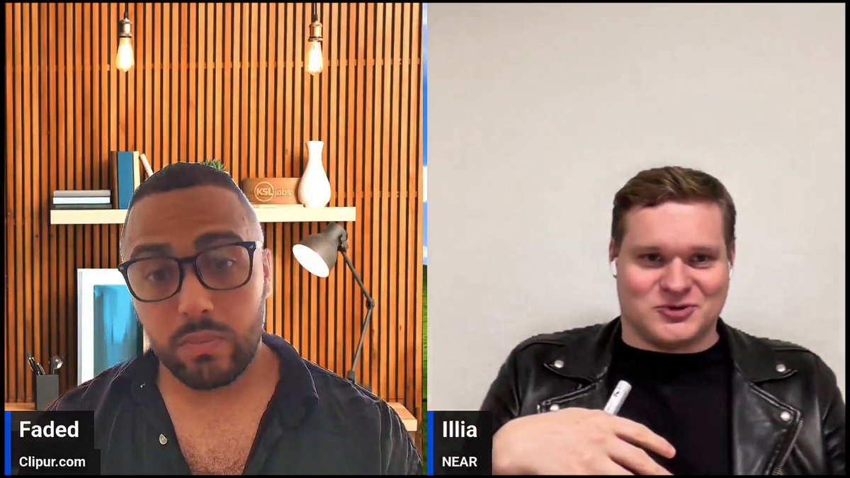 The image shows two men having a video call, with one man wearing glasses and holding a white object while talking to another man who is not wearing glasses but has a black jacket on. The background of the image features wooden panels, which adds an interesting visual element to the scene.