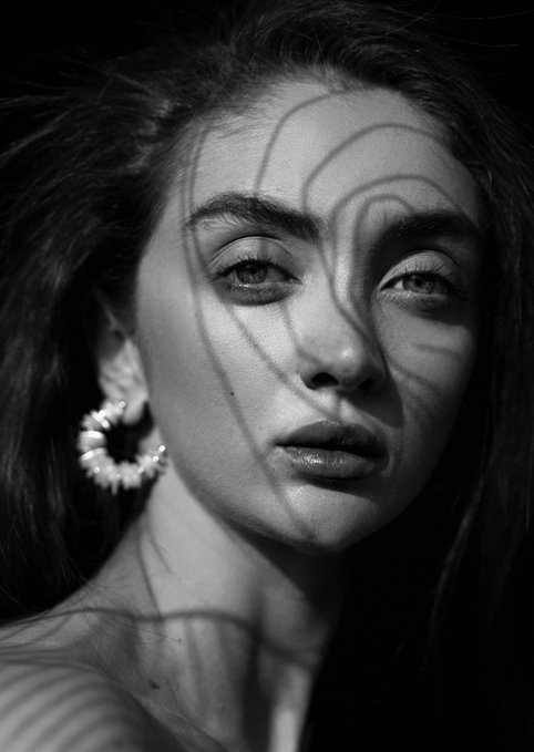 A black and white portrait of a woman with swirl-patterned light shadows cast across her face and ear.