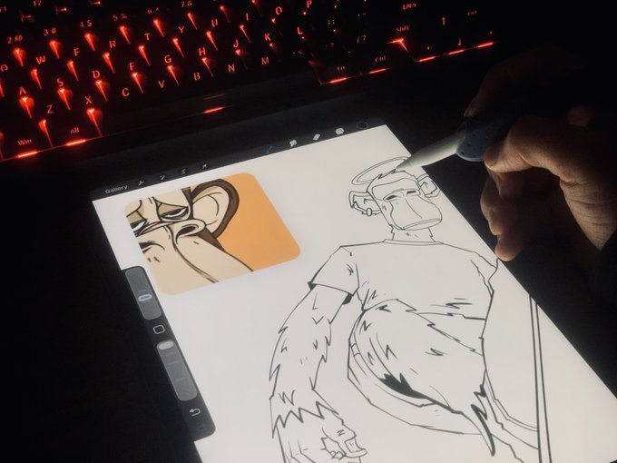 A close-up of a digital drawing tablet in a dimly lit room, with a hand using a stylus to draw a character; a red-backlit keyboard is visible in the background.