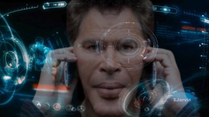 A scene from a movie showing a man wearing a futuristic transparent heads-up display (HUD) with digital interfaces overlaid on his vision, resembling the JARVIS system from an Iron Man movie.