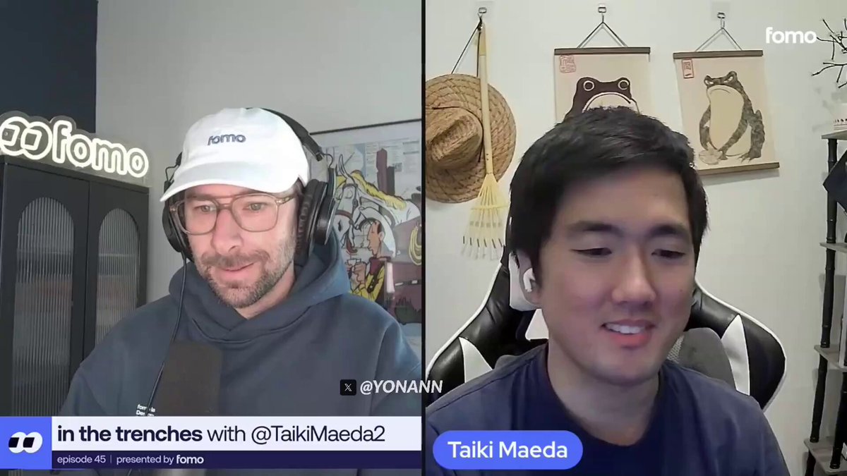 The image shows a conversation between two men wearing headphones while sitting in chairs. One man has a white hat on, and they appear to be talking about cryptocurrency or crypto trading. The other man is smiling at the camera, indicating that he is engaged in the discussion.