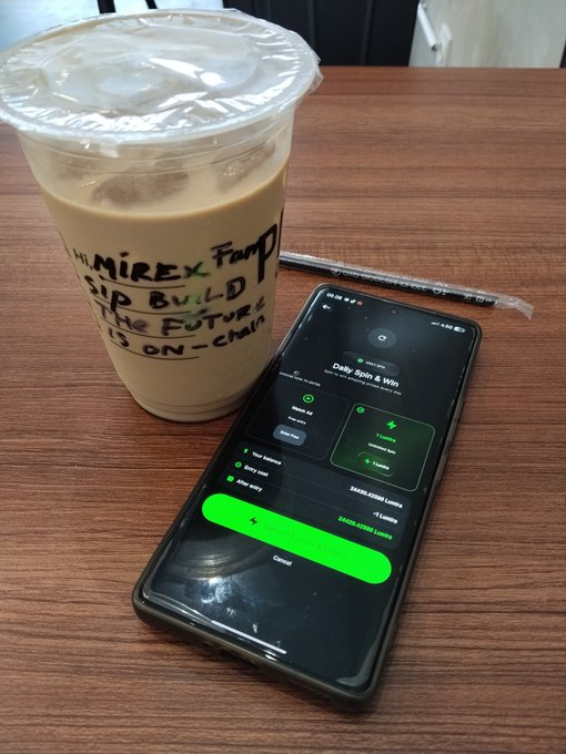 An iced coffee in a cup labeled 'MINIREX' sits on a wooden table next to a smartphone displaying a 'Daily Spin & Win' rewards screen.